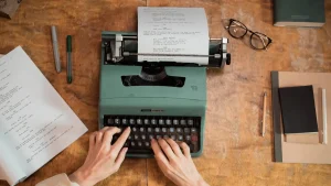 hands typing on a typewriter at a writing desk