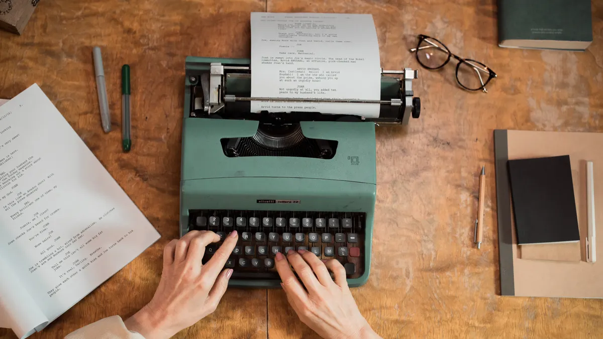 hands typing on a typewriter at a writing desk