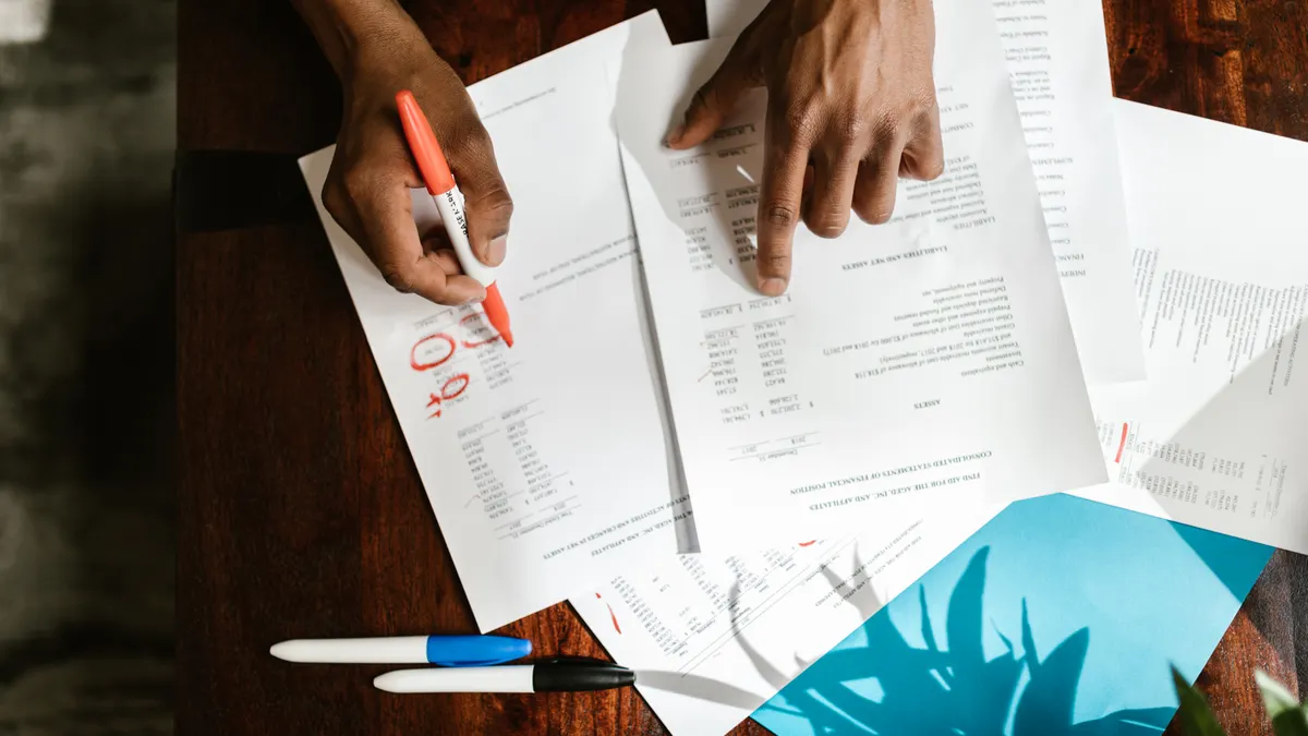 Multiple hands reviewing marked-up printed pages