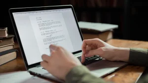 hands typing on laptop beside a written document