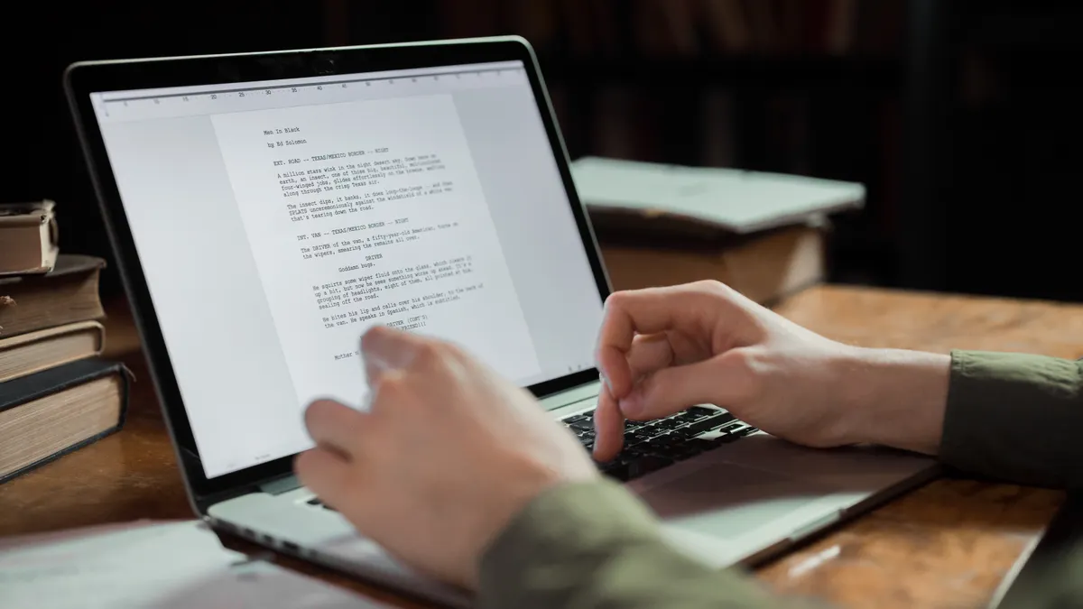 hands typing on laptop beside a written document